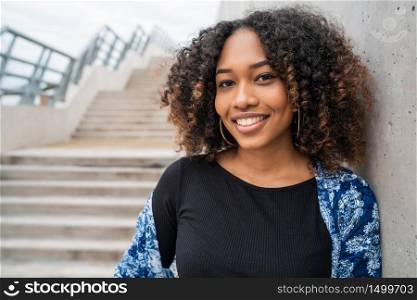 Portrait of beautiful young afro-american woman with curly hair standing against concrete stairs outdoors.