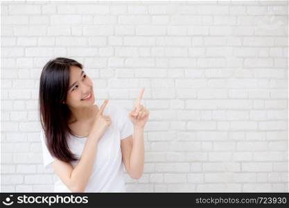 Portrait of beautiful young asian woman happiness standing finger pointing something on gray cement texture grunge wall brick background, businesswoman is a smiling on concrete, business people concept.