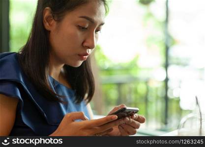 Portrait of beautiful young asian woman reading messages on her smartphone in coffee shop