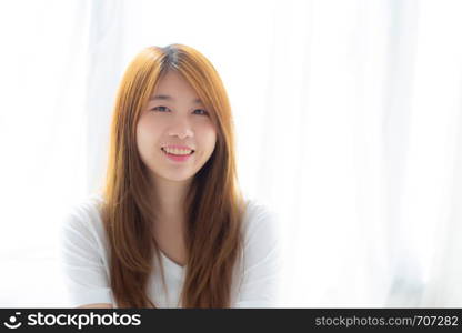 Portrait of beautiful young asian woman standing the window and smile while wake up with sunrise at morning, lifestyle and relax concept.