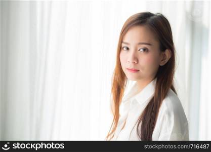 Portrait of beautiful young asian woman standing the window and smile while wake up with sunrise at morning, lifestyle and relax concept.