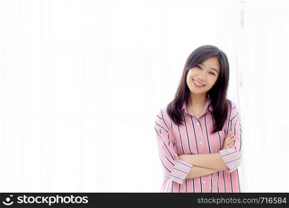 Portrait of beautiful young asian woman standing the window and smile while wake up with sunrise at morning, lifestyle and relax concept.