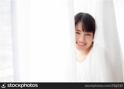 Portrait of beautiful young asian woman standing the window and smile while wake up with sunrise at morning, girl happy with freshness and cheerful, lifestyle and relax concept.