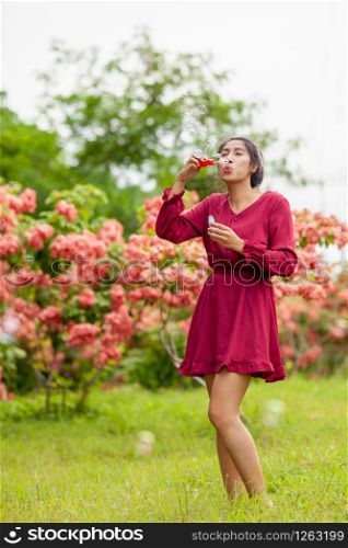 Portrait of beautiful young asian woman with Carmen red dress blowing bubble in the park