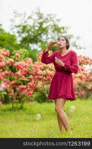 Portrait of beautiful young asian woman with Carmen red dress blowing bubble in the park