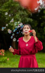 Portrait of beautiful young asian woman with Carmen red dress blowing bubble in the park