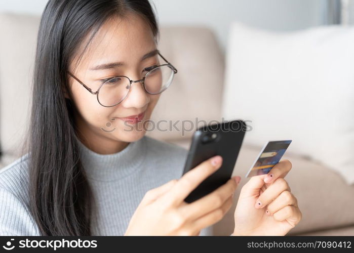 portrait of Beautiful young Asian women are buying online with a credit card. asia girl are using smartphone and making online transactions in the living room at home.