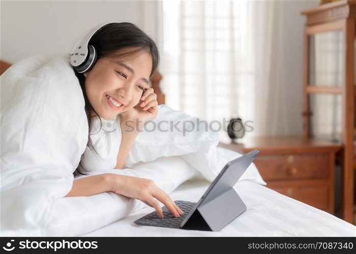 portrait of Beautiful young Asian women is resting listening to music on bed with earphone. Asia girl using tablet for entertainment at home