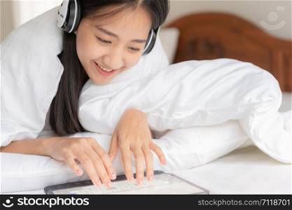 portrait of Beautiful young Asian women is resting listening to music on bed with earphone. Asia girl using tablet for entertainment at home