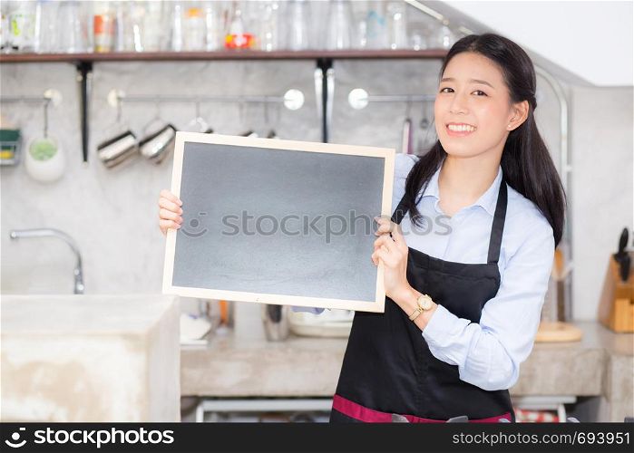 Portrait of beautiful young barista, asian woman is a employee standing holding chalkboard in counter coffee shop, service concept.