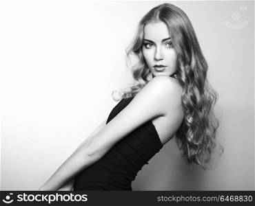 Portrait of beautiful young blonde girl in black dress. Fashion photo. Long Hair
