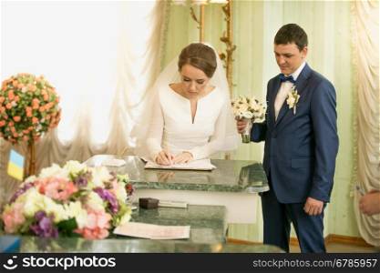Portrait of beautiful young bride signing wedding license at registry office