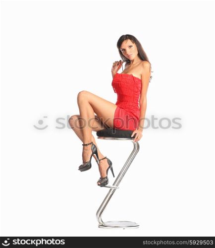 Portrait of beautiful young brunette woman in stylish red dress and court shoes sitting on bar chair.