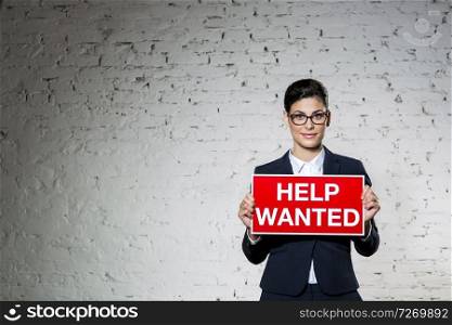 Portrait of beautiful young businesswoman holding help wanted sign against brick wall