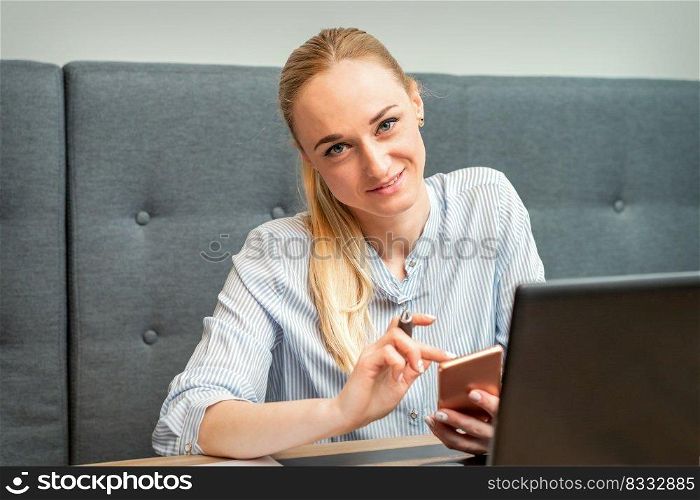 Portrait of beautiful young caucasian businesswoman with smartphone working in office looking and smiling at camera. Businesswoman with smartphone working in office