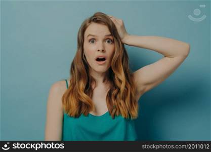 Portrait of beautiful young caucasian woman with surprised and shocked look being amazed with wide open eyes and mouth isolated on blue studio background. Human facial expressions and emotions concept. Surprised and shocked caucasian woman being amazed with wide open eyes and mouth, isolated on blue
