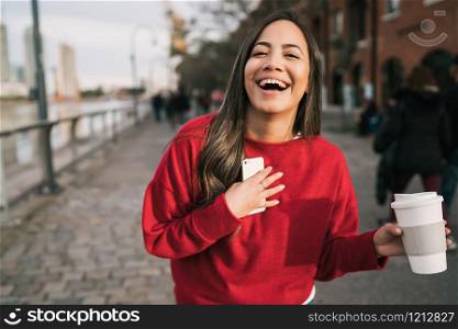 Portrait of beautiful young confident woman happy and excited holding a cup of coffee outdoors in the street.