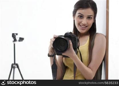 Portrait of beautiful young female holding camera with tripod behind