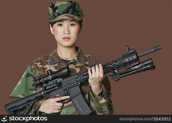 Portrait of beautiful young female Marine Corps soldier holding M4 assault rifle over brown background