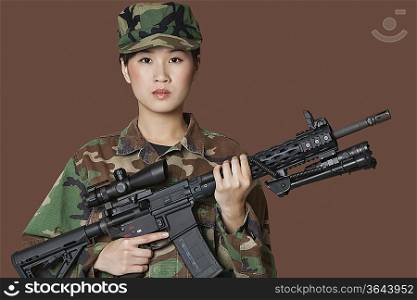 Portrait of beautiful young female Marine Corps soldier holding M4 assault rifle over brown background