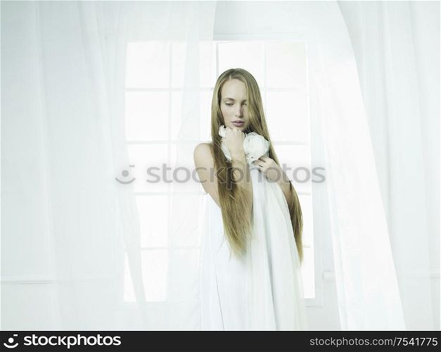 Portrait of beautiful young girl in the white interior in front of the window