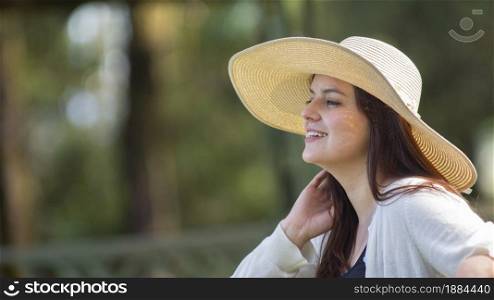 Portrait of beautiful young Hispanic woman with long hair with a hat very cheerful sitting on a park bench against a background of unfocused green trees during sunset. Portrait of beautiful young Hispanic woman with long hair with a hat very cheerful sitting on a park bench against a background of unfocused green trees