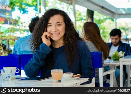 Portrait of beautiful young latin woman talking on mobile phone at coffee shop.