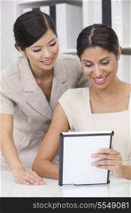 Portrait of beautiful young mixed race Hispanic woman or businesswoman in office meeting with Chinese Asian female colleague using a tablet computer