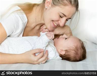 Portrait of beautiful young mother cuddling her baby boy on bed