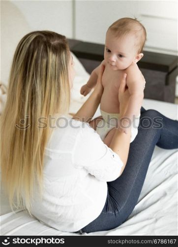 Portrait of beautiful young mother sitting on bed with her 6 month old son