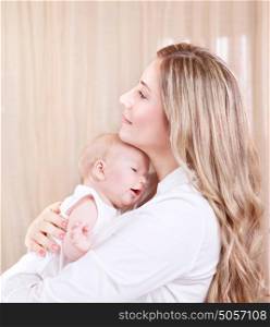 Portrait of beautiful young mother with adorable newborn daughter on hands, spending time at home, happy motherhood, love concept