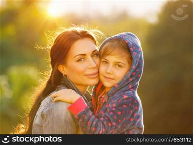 Portrait of beautiful young mother with her cute little daughter outdoors in bright sun light, spending time together in the park, happy loving family