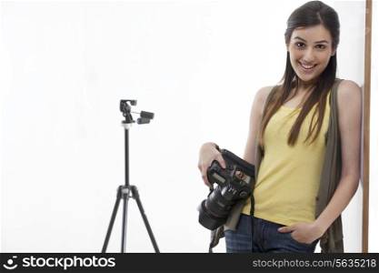 Portrait of beautiful young photographer with digital camera leaning against wall