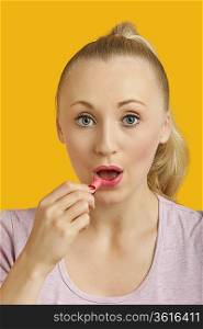 Portrait of beautiful young woman applying lipstick over yellow background