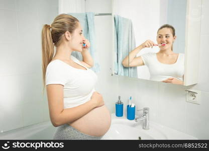 Portrait of beautiful young woman brushing teeth at mirror in bathroom