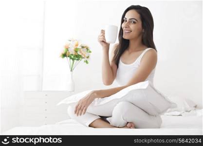 Portrait of beautiful young woman drinking coffee on bed
