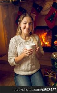 Portrait of beautiful young woman drinking tea at the fireplace