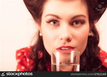 Portrait of beautiful young woman drinking water from glass. Girl with pinup makeup and hairstyle on pink. Studio shot. Retro style.