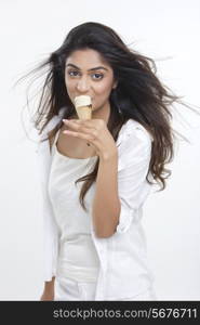 Portrait of beautiful young woman eating ice cream cone over white background