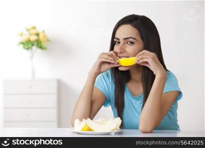 Portrait of beautiful young woman eating slice of melon at home