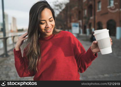 Portrait of beautiful young woman holding a cup of coffee outdoors. Urban concept.