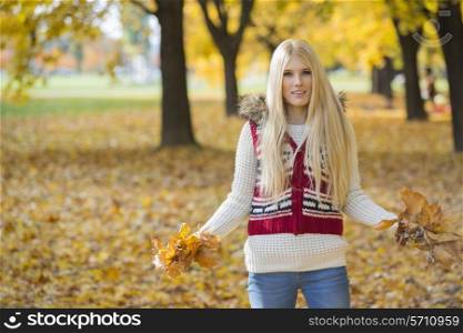Portrait of beautiful young woman holding autumn leaves in park