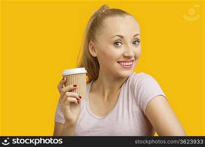 Portrait of beautiful young woman holding disposable cup over yellow background