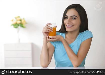 Portrait of beautiful young woman holding glass of orange juice at home