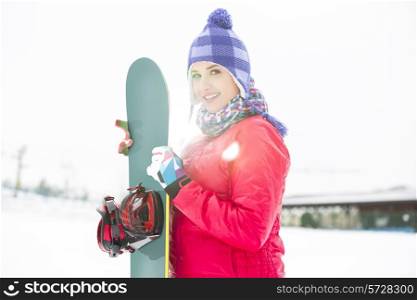 Portrait of beautiful young woman holding snowboard in snow