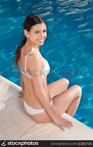 Portrait of beautiful young woman in a bikini sitting around a swimming pool