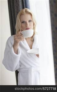 Portrait of beautiful young woman in bathrobe drinking coffee at hotel room