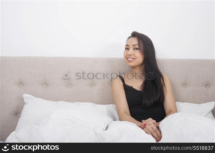 Portrait of beautiful young woman in nightwear sitting on bed