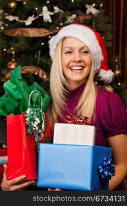 Portrait of beautiful young woman in Santa hat smiling while holding gift boxes.