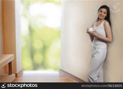 Portrait of beautiful young woman leaning on wall while holding cup of coffee